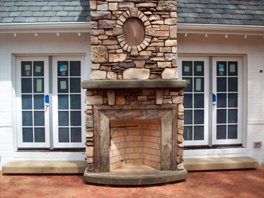 камин с металлической топкой, облицованный  бутом и  обрамлённый окорёнными  стволами  деревьев 